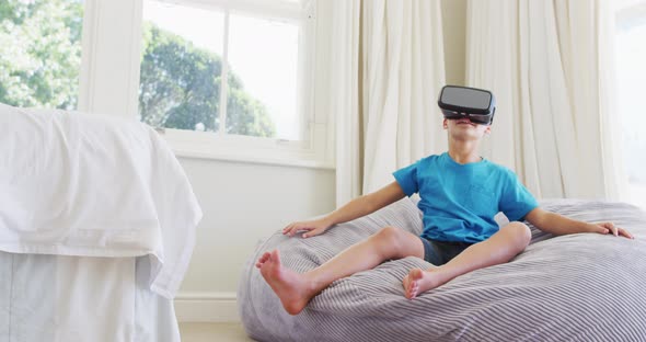 Caucasian boy wearing vr headset while sitting on the bean bag at home alt
