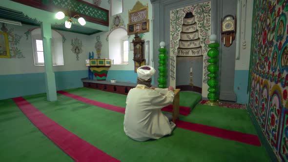 Muslim Mosque Teacher is reading the Quran in Small Historic Wooden Masjid alt