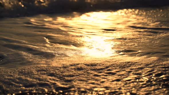 Closeup of Sea Waves Reflecting Sunset Sunlight Hitting Sandy Beach
