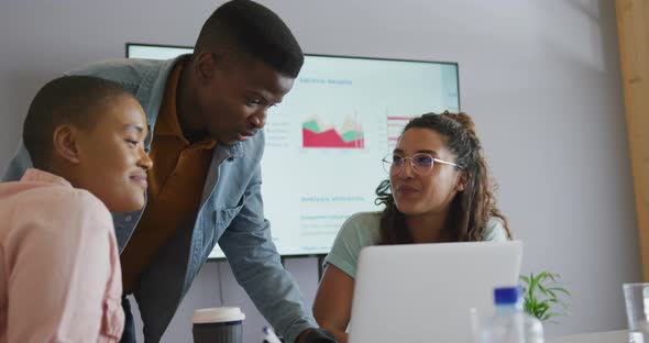 Three diverse creative male and female colleagues in discussion at meeting using laptop and screen alt
