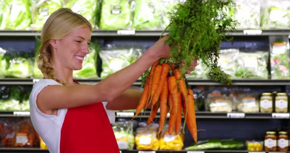 Smiling staff holding bunch of carrots in organic section alt