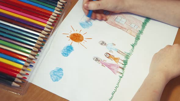 A Child's Hand Draws Blue Clouds Above the Family Next to the House alt