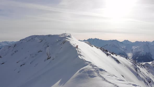 Drone flies towards snowboarder walking on thin ridge in Austria to get first tracks alt