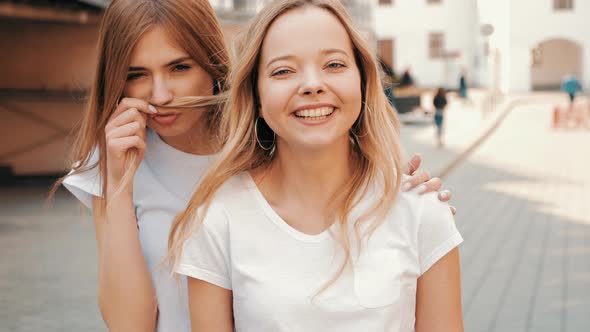 Two young beautiful blond smiling hipster girls in trendy summer clothes alt