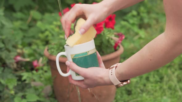 Women's hands wash a glass glass under water from a tap outdoors.