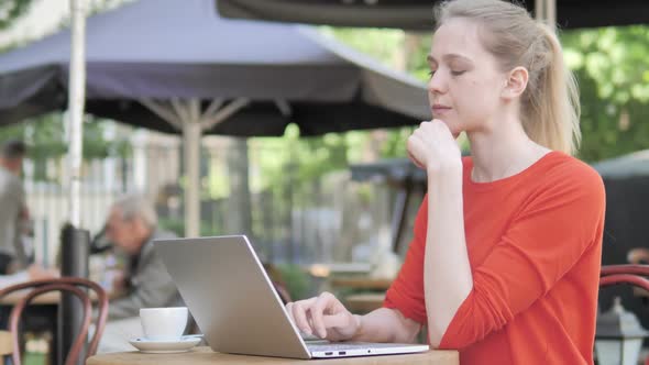 Pensive Young Woman Working on Laptop Sitting in Cafe Terrace alt
