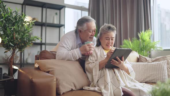 old senior asian retired couple enjoy video calling conversation together to family on sofa