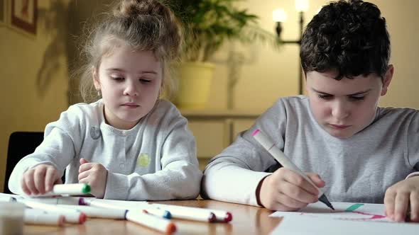 Small preschool girl with brother enthusiastically draws with colored pencils.