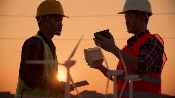 Asian engineer discussion about home solar cell farm and wind turbine model in construction site