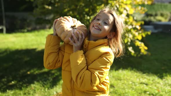 An orange pumpkin in the hands of a girl in the autumn park