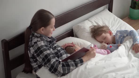 Authentic Cute Young Woman or Babysitter Reads Fairy Tale From Book to Children Before Bedtime alt