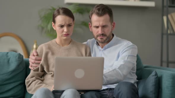 Couple Reacting to Loss on Laptop While Sitting on Sofa alt