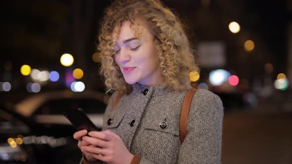 Woman Is Chatting in the Smartphone Against the Background of the Evening City