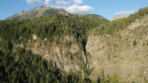 Aerial dolly left flying over Corbata Blanca waterfall hiding between mountains covered in pine tree alt