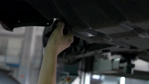 Worker Mechanic Unscrewing Parts of Automobile's Bottom Under Lifted Car alt