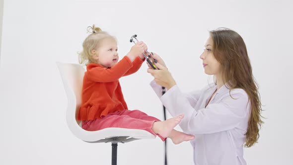 Playfully Little Girl Sits on Chair Checking Doctor's Breath with Stethoscope