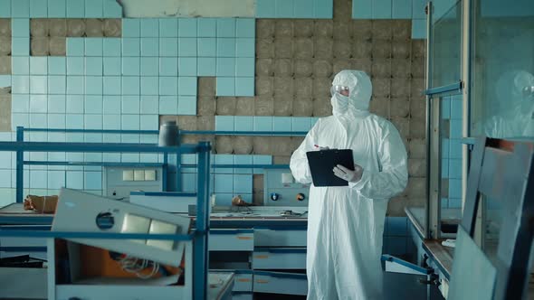 The lab assistant in a protective suit and glasses holds a folder with documents