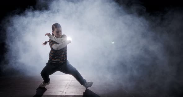 silhouette of a dancer performing hip hop dance in slow motion with light and smoke background alt