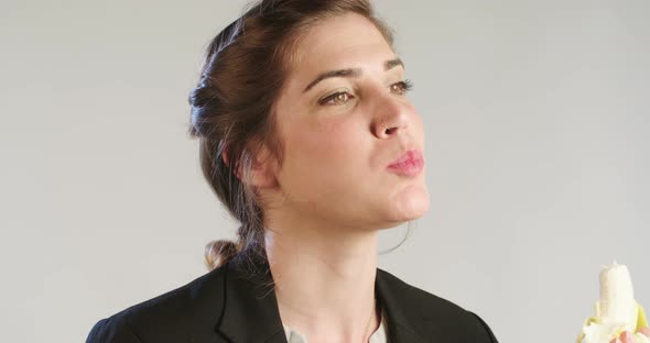 Close up of a woman eating a banana on a white studio background alt