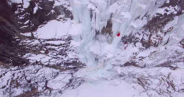 Aerial drone view of a man ice climbing on a frozen waterfall in the mountains alt