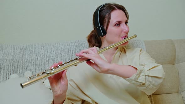 A woman with a flute is playing at home on the sofa in the living room