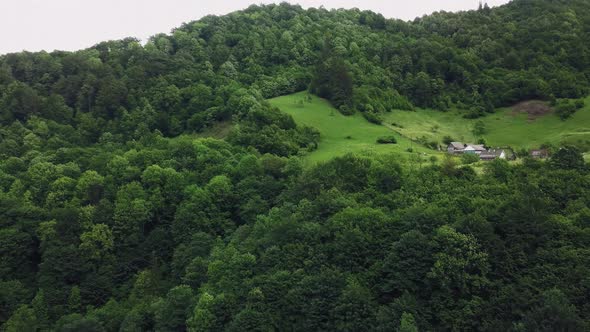 Aerial Drone Footage View: Flight over summer mountain village with forests, fields and river in sun