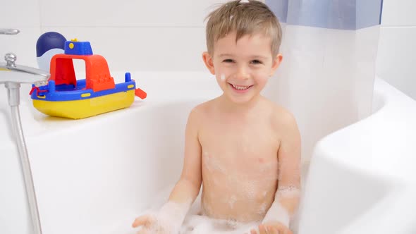 Slow Motion of Cheerful Laughing Little Boy Splashing Water and Foam While Taking Bath, Stock Footage