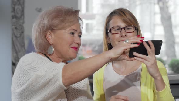 Elderly Mother and Her Mature Daughter Taking Selfies Together Using Smart Phone alt