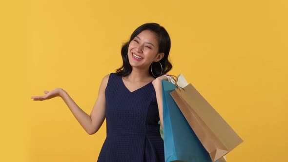 Asian woman holding colorful shopping bags pointing to empty space and open palm
