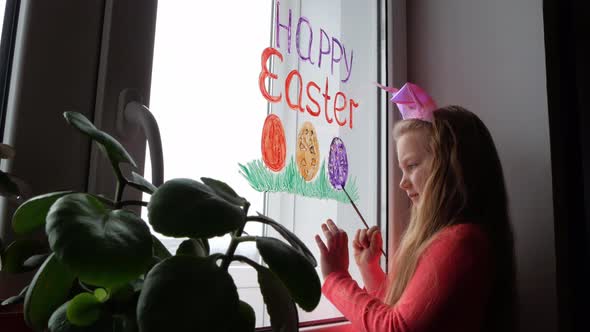 Cute little girl in bunny ears painting Easter eggs with green spring grass on window at home alt