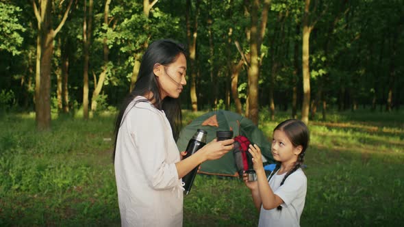 Happy Asian Woman Enjoys Vacation with Her Daughter Walking Along the Forest Path Drinking Tea From alt