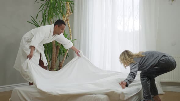 Wide Shot of Happy Smiling Couple Making Bed and Lying Down Talking alt