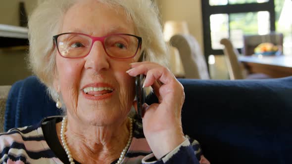Senior woman talking on mobile phone in living room 4k alt