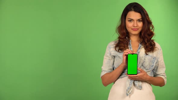 A Caucasian Woman Shows a Smartphone with Green Screen to the Camera with a Smile  Green Screen