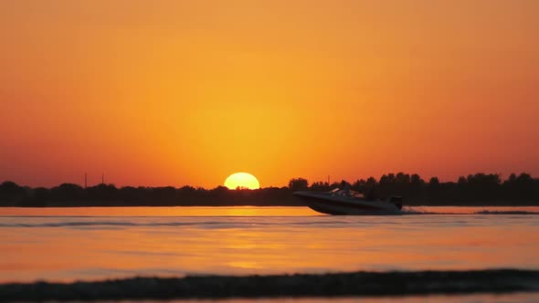 Sunset Over the River and Silhouette of Motor Boat with Wakeboarder. Slow Motion