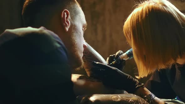 Woman Tattoo Artist at Work with Man Customers Arm alt