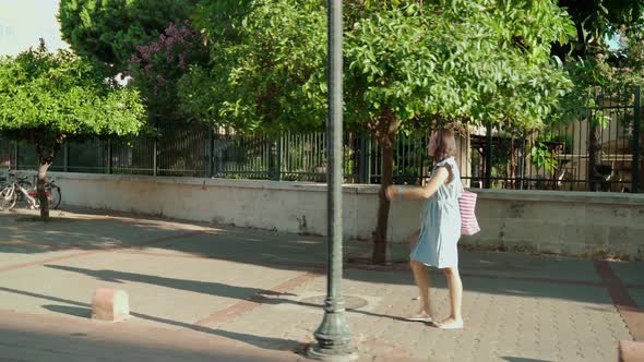 A Woman with a Bag on Her Shoulder Walks Along a Deserted Street at Dawn alt