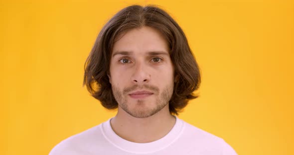 Studio Portrait of Young Caucasian Man Looking Seriously at Camera, Orange Background alt