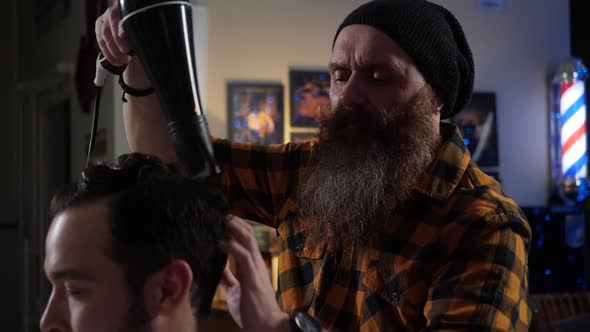 Adult Male Barber with a Long Beard Dries with a Hairdryer and Puts Hair