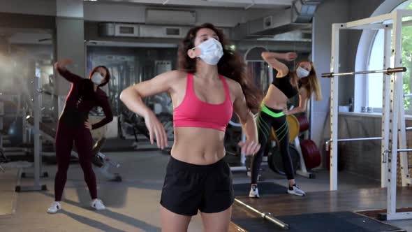 A Group of Athletic Women Wearing Protective Masks Warm Up and Stretch in the Gym. 