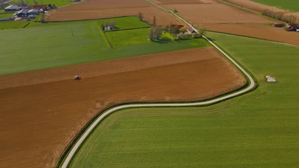 Aerial view of the countryside. A tractor plows the field next to the road. The village and the chur alt