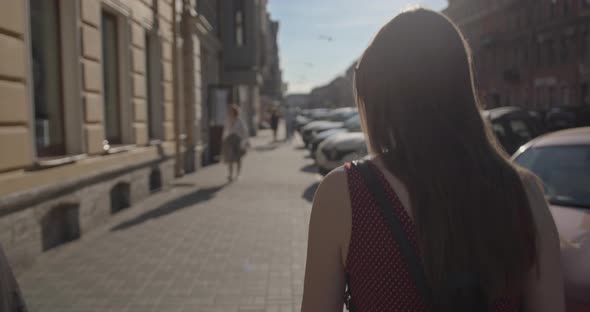 A Young Beautiful Girl in a Dress Walks Along a City Street