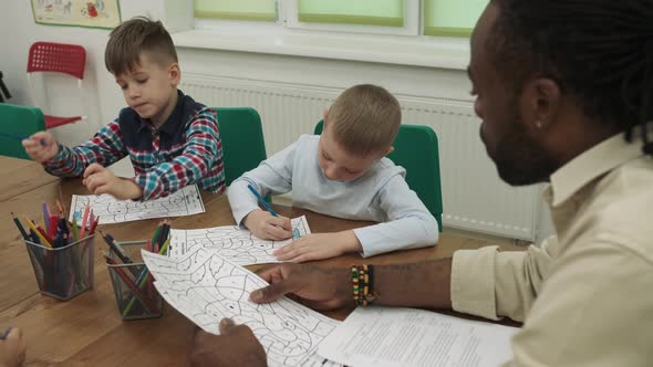 An African American Teacher Teaches a Group of Children to Draw While Sitting at a Table in the alt