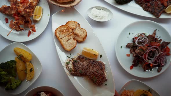 Overhead View of a Hand Serving Meat and Grilled Bread Dish on a White Plate alt