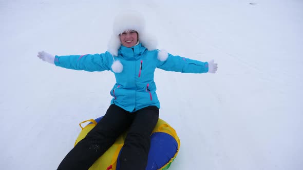 Beautiful Young Woman Slides Slide in Snow on an Inflatable Snow Tube and Waves Hand. Happy Girl alt
