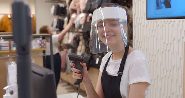 Woman Seller in Plastic Face Shield Holding Scanner and Standing at Checkout in Store alt
