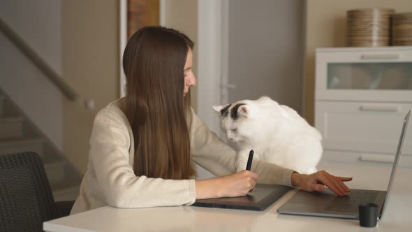 Young Female Adult Designer with Stylus and Pet Tablet Plays with Cat at Home