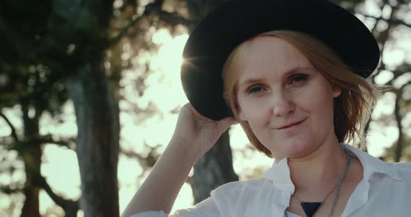 Portrait of a Woman in a Hat Stands Against the Background of the Forest alt