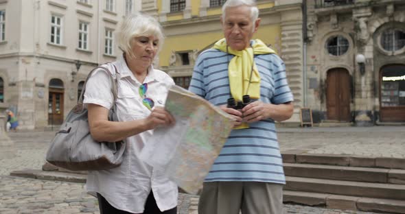 Senior Male and Female Tourists Walking with a Map in Hands Looking for Route alt