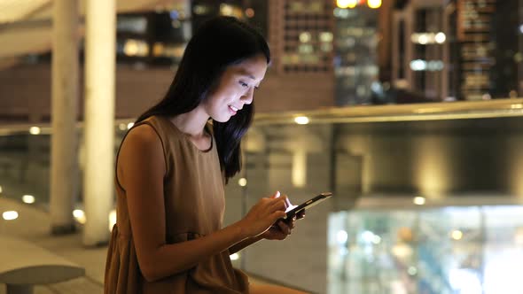 Woman looking at mobile phone in city at night  alt